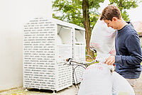 Frau spendet Klamotten an DRK-Kleidercontainer