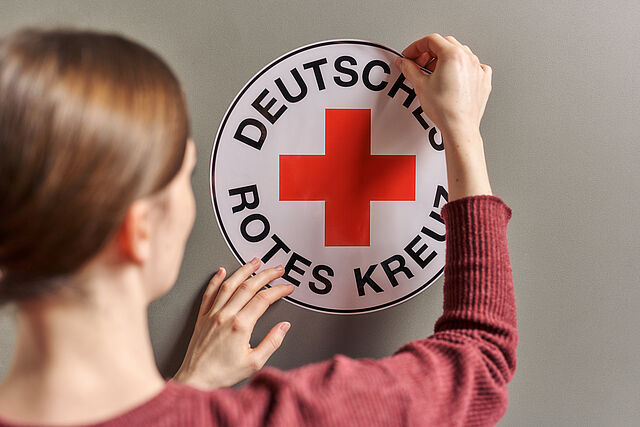Frau klebt Aufkleber vom Deutschen Roten Kreuz auf Wand