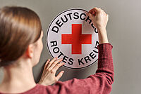 Frau klebt Aufkleber vom Deutschen Roten Kreuz auf Wand